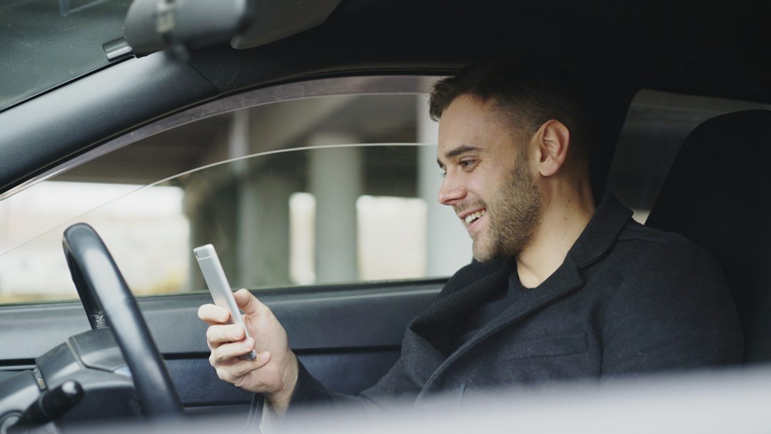 Homem sorrindo dentro do carro enquanto consulta informações no celular